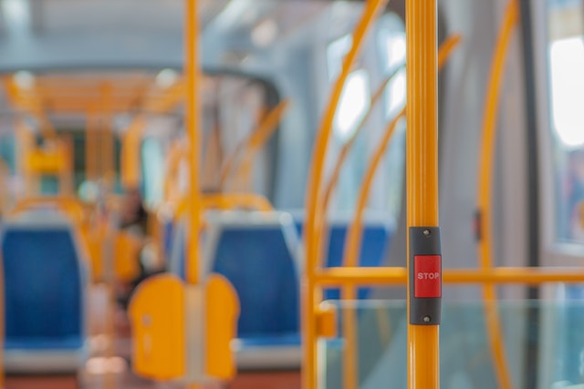 Inside of a brightly lit bus with seats, poles and a stop button. 