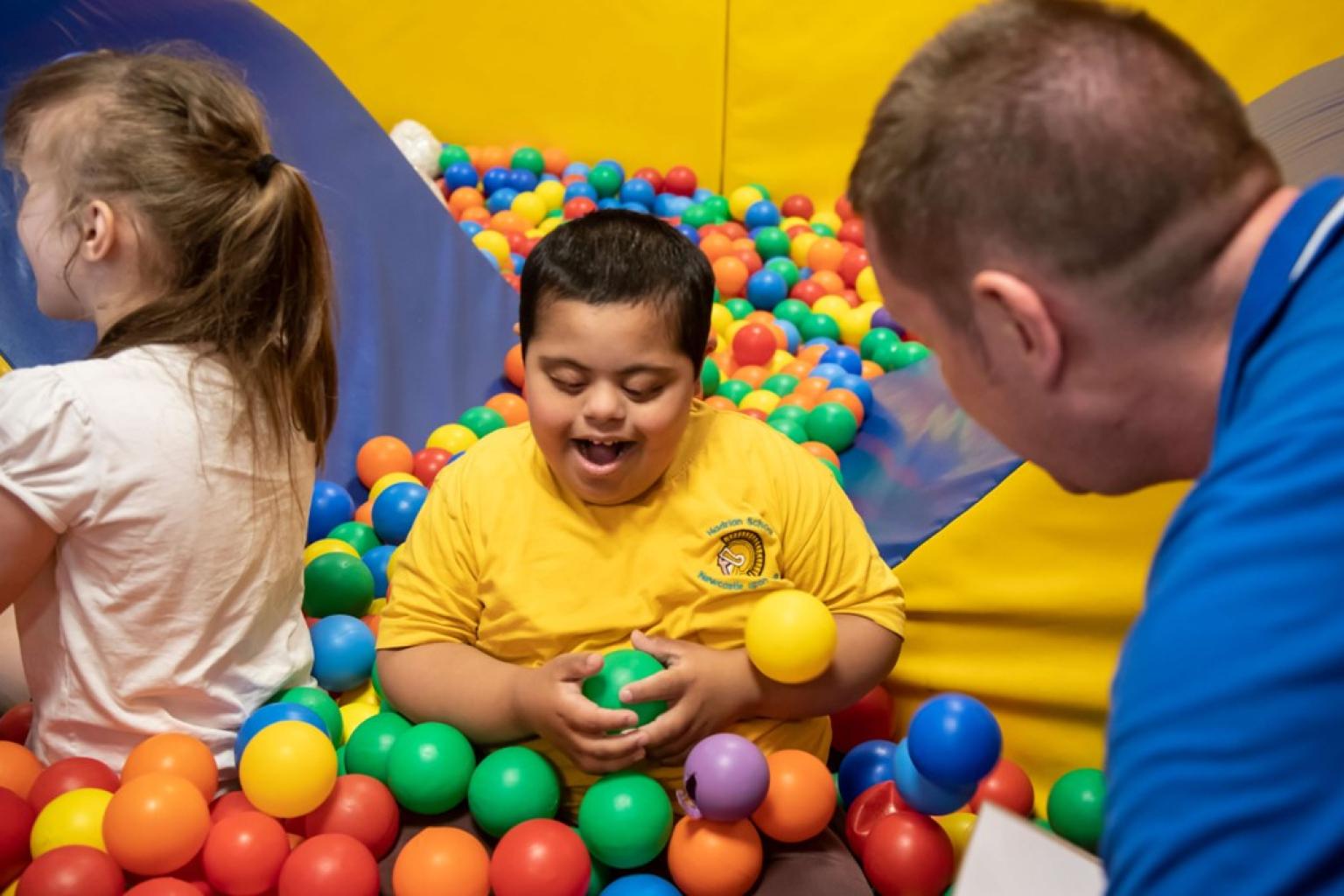 A smiling boy in a yellow t-shirt playing in a colourful ball pit