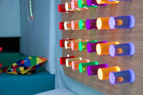 A row of colourful lit up cylinders on a wall in a sensory room. 