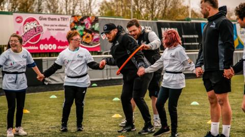 Men and young people holding hands playing a team building game with a hoop.