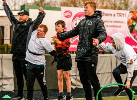 A group of boys and men wearing sporty clothes and cheering while outside.