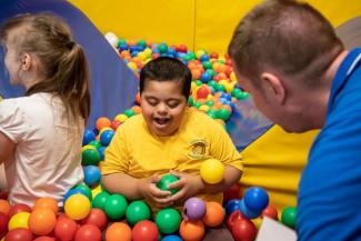 A smiling boy in a yellow t-shirt playing in a colourful ball pit